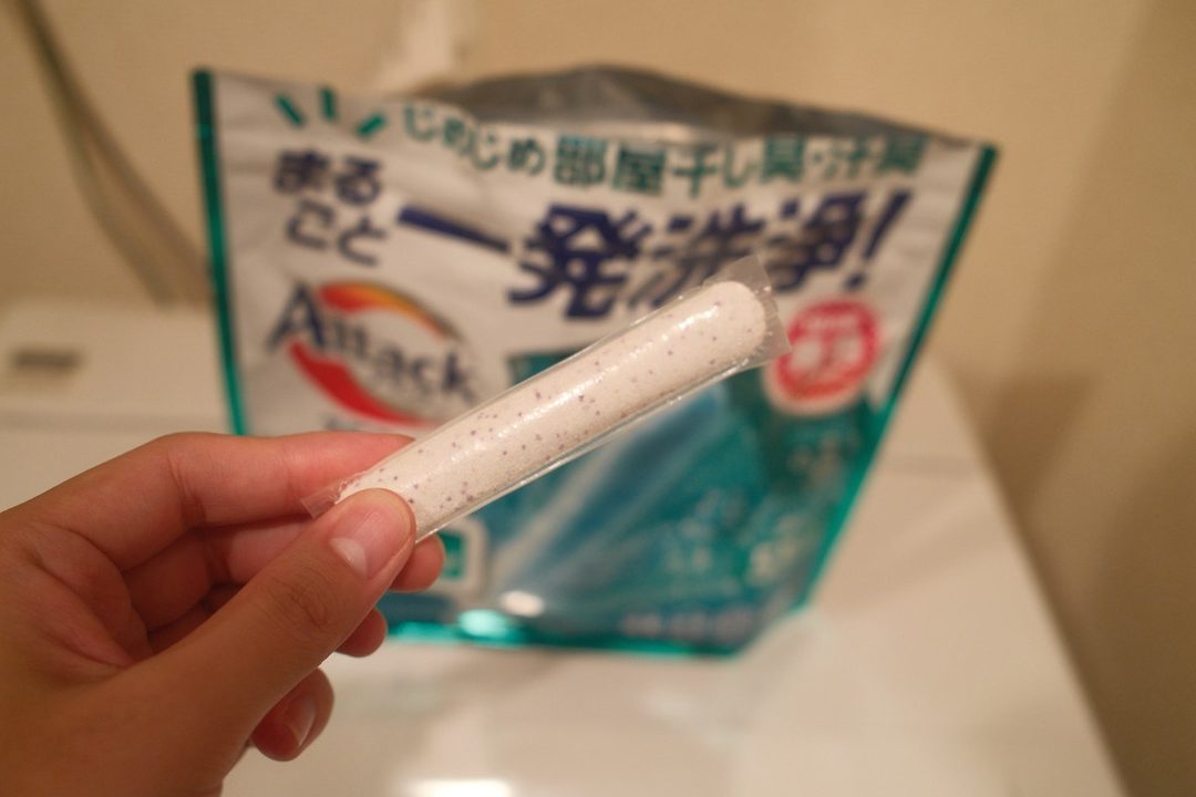 アタックZERO パーフェクトスティックを1本、袋の前で手に持ったところ。白い粉に紫の粒が混ざっている